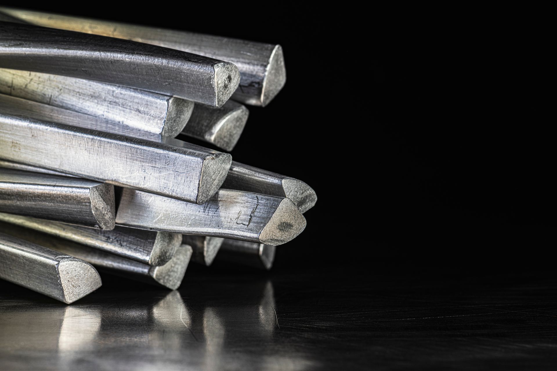 Stack of metal rods or bars arranged on a dark surface against a black background. Stack of metal rods or bars arranged on a dark surface against a black background.