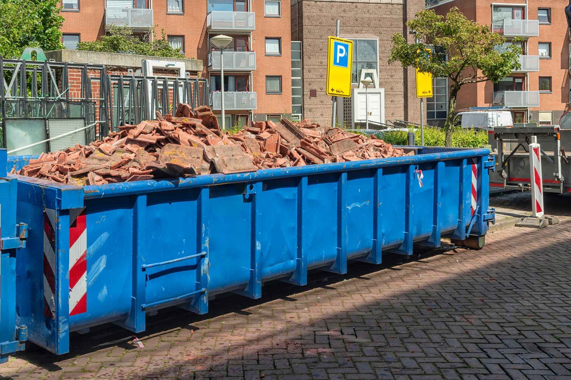 A blue dumpster filled with bricks is parked on the side of the road.