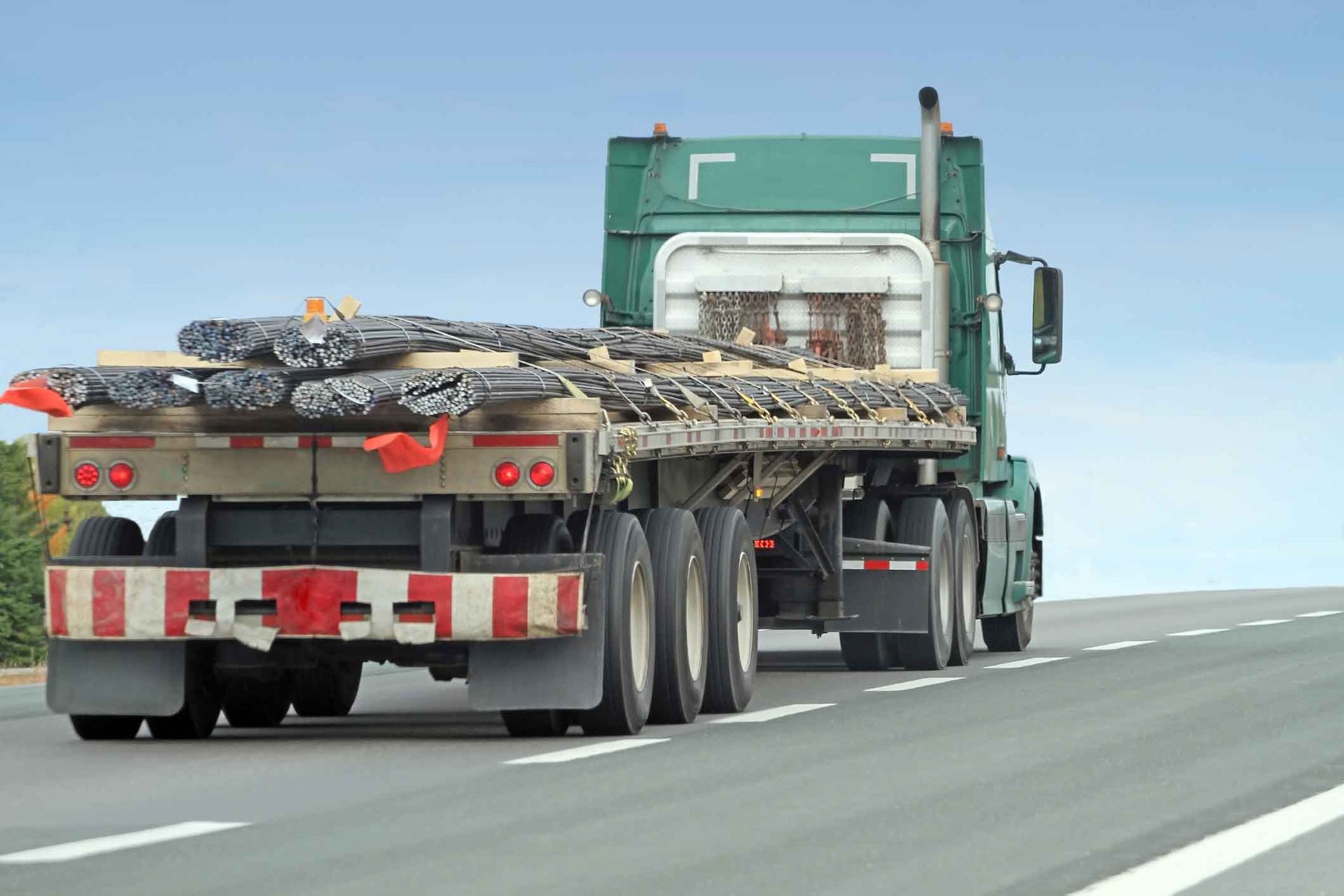 A semi truck with a flatbed is driving down a highway.