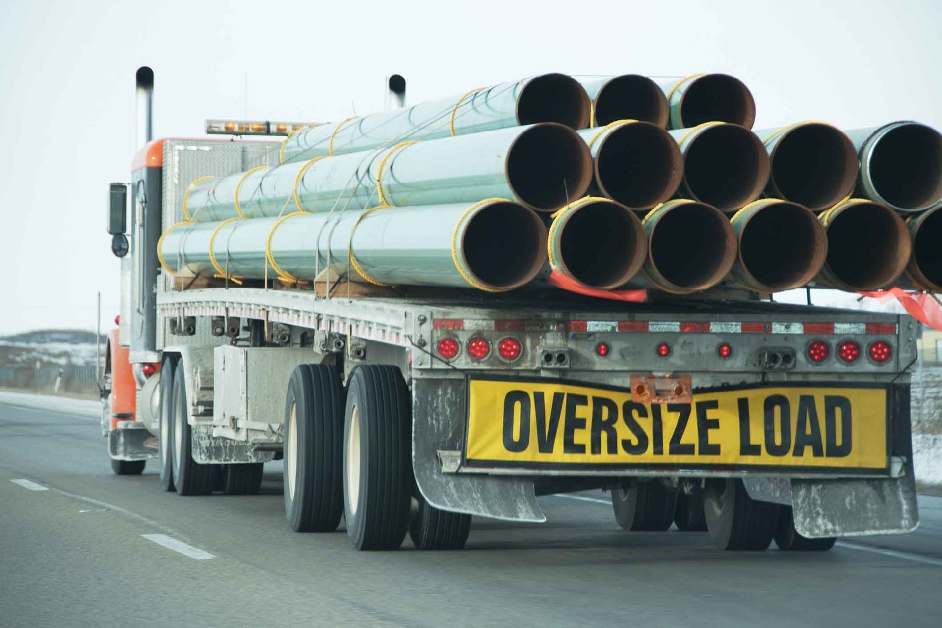 A semi truck is carrying a large amount of pipes on the back of it.