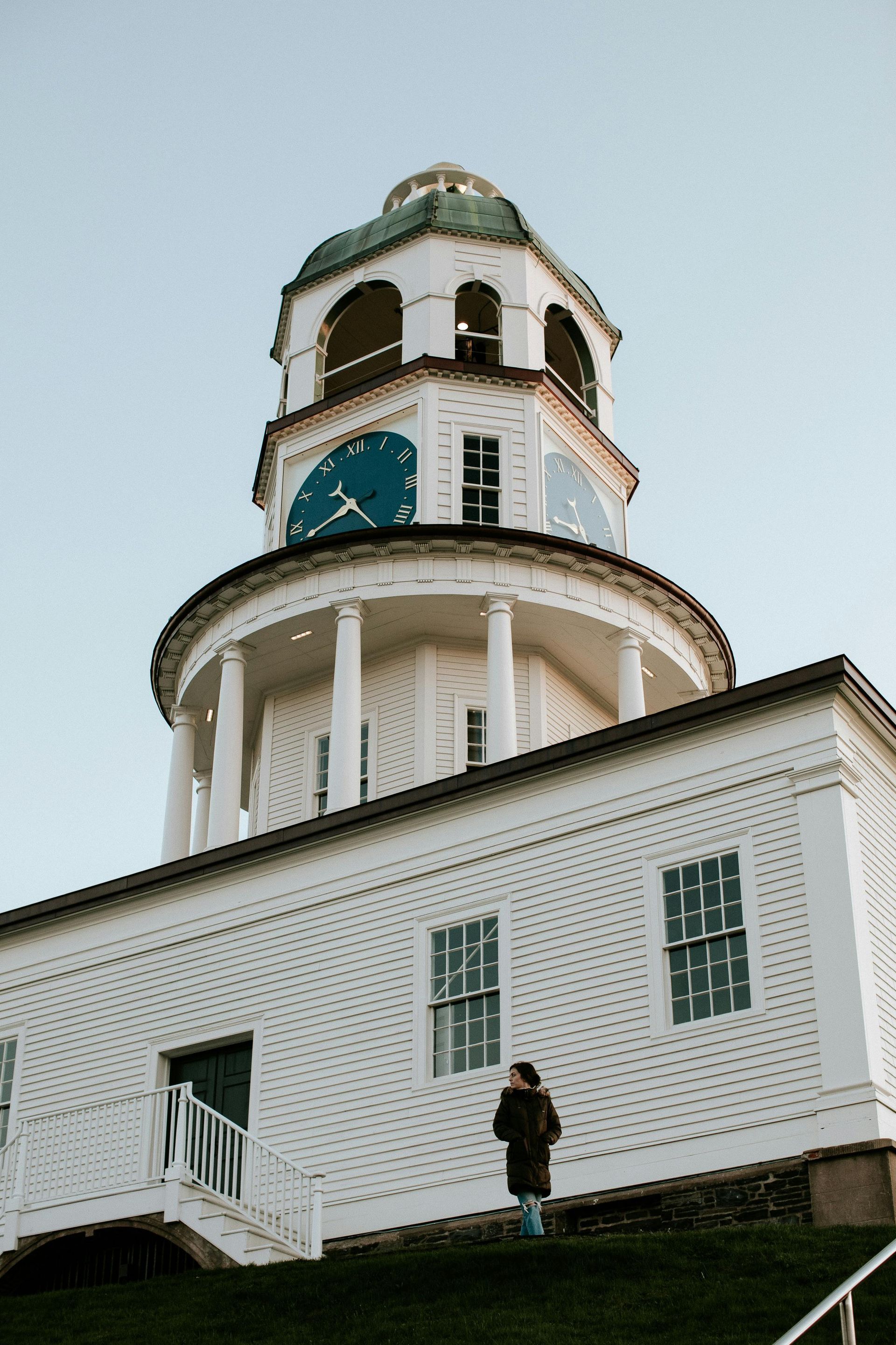 Citadel Hill clock tower with blue clock faces, a person standing on the hill in Halifax, NS