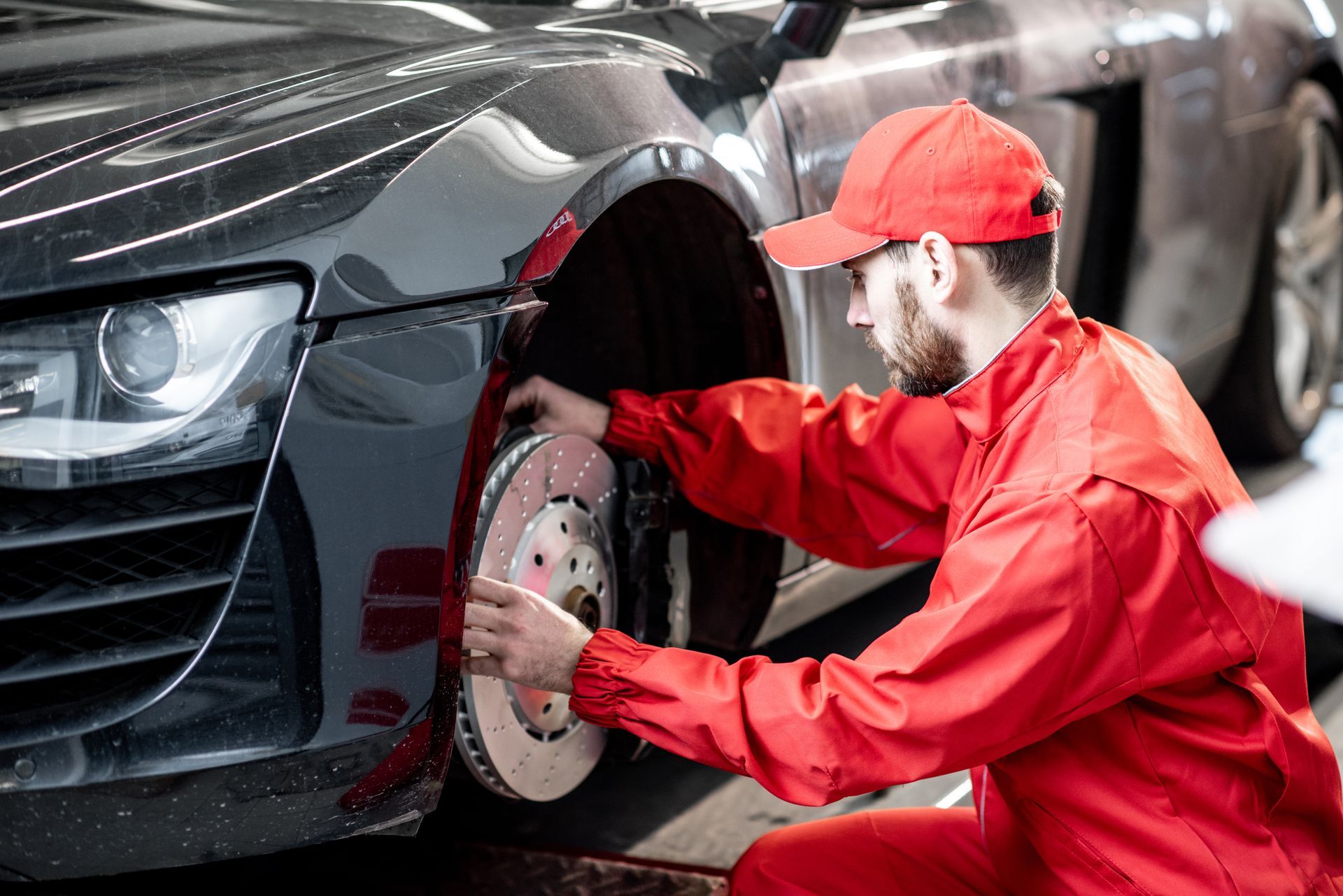 A mechanic in a red uniform is performing Mercedes-Benz auto repair, checking the front brakes.