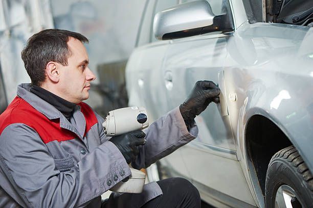 Auto body technician using heat gun to repair dent on car door during vehicle bodywork service task