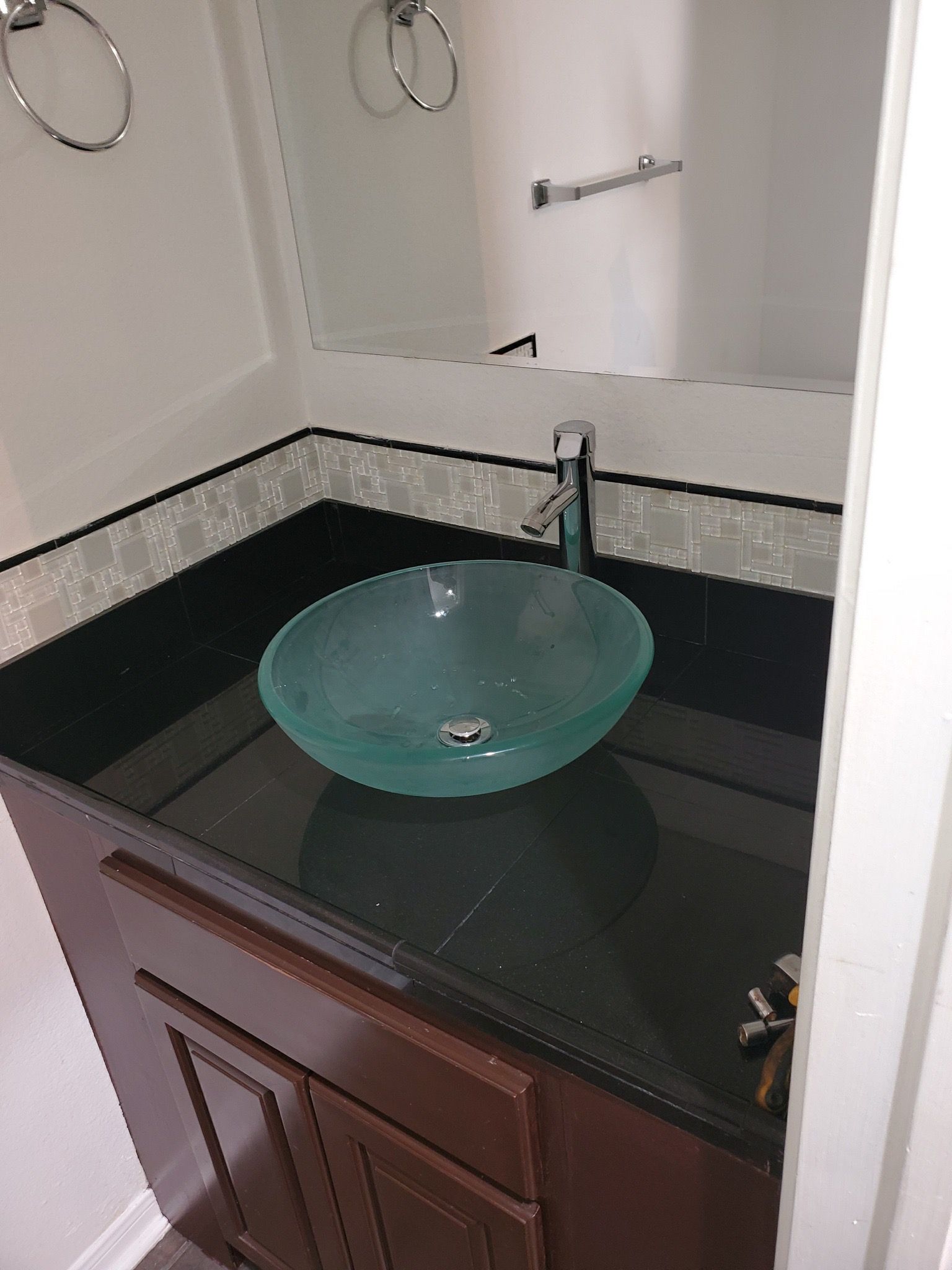 Bathroom vanity with a glass bowl sink, dark countertop, brown cabinet, and chrome fixtures.