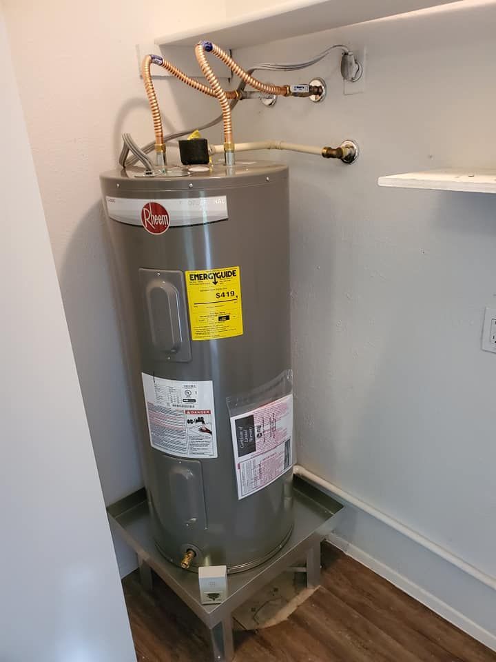 A Rheem water heater on a metal stand inside a utility closet. Copper pipes connect to the top.