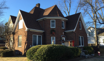 A bright bathroom featuring a white clawfoot bathtub centered under two windows, a vanity, and a white wicker chair.