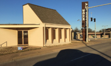 A bright bathroom featuring a white clawfoot bathtub centered under two windows, a vanity, and a white wicker chair.