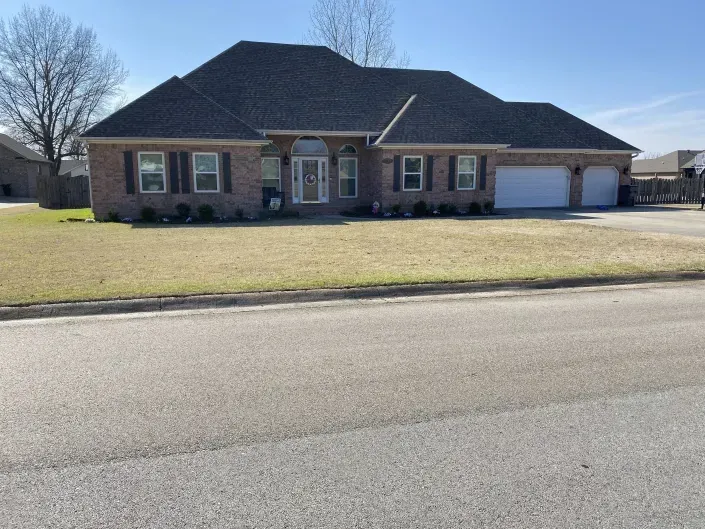 A brick, single-story suburban house with a gray shingled roof, arched front entryway, and an attached two-car garage.