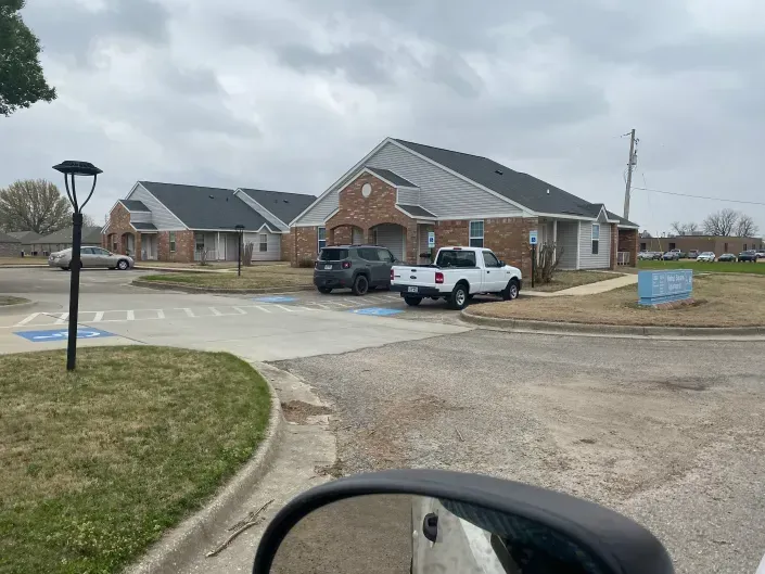 A brick office building with a parking lot containing a gray SUV and a white pickup truck, seen from a vehicle.