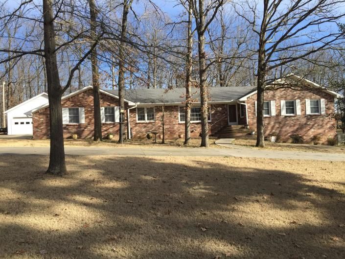 A one-story brick house with a detached white garage, surrounded by bare trees under a blue sky.