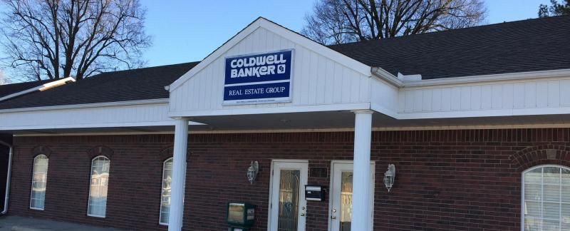 A Coldwell Banker Real Estate Group office building with a dark brick exterior, white columns, and a white entrance roof.