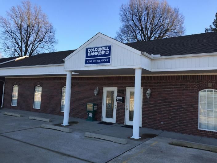 A single-story brick commercial building with a Coldwell Banker sign above the entrance and a concrete parking lot.