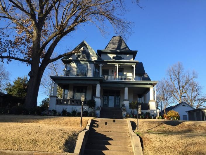 A large, two-story Victorian house with a front porch, a turret, and a concrete staircase leading up from a lawn.
