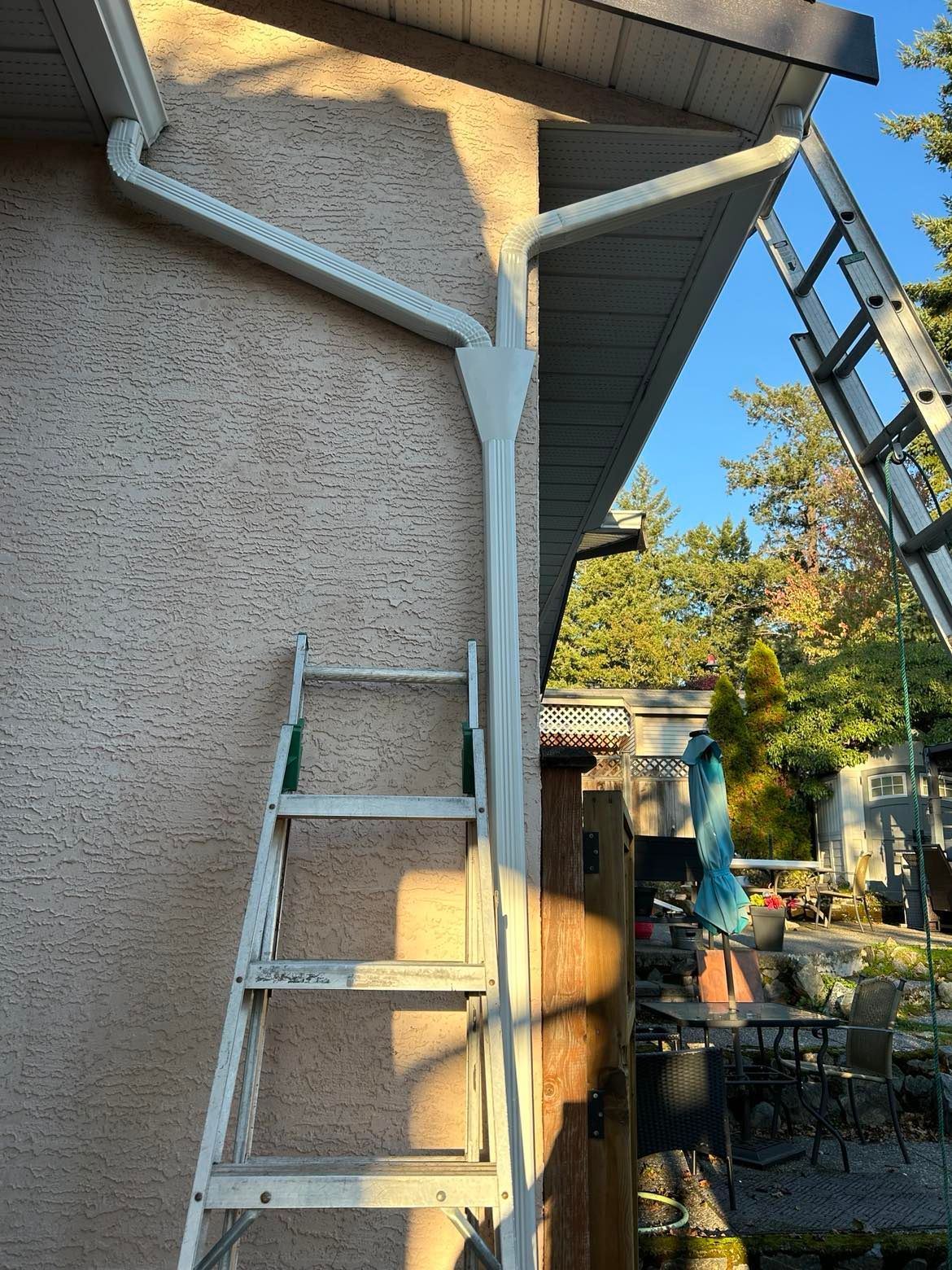 2 downspouts running water from 2 different gutters, connected using a funnel, running into 1 drain tile.