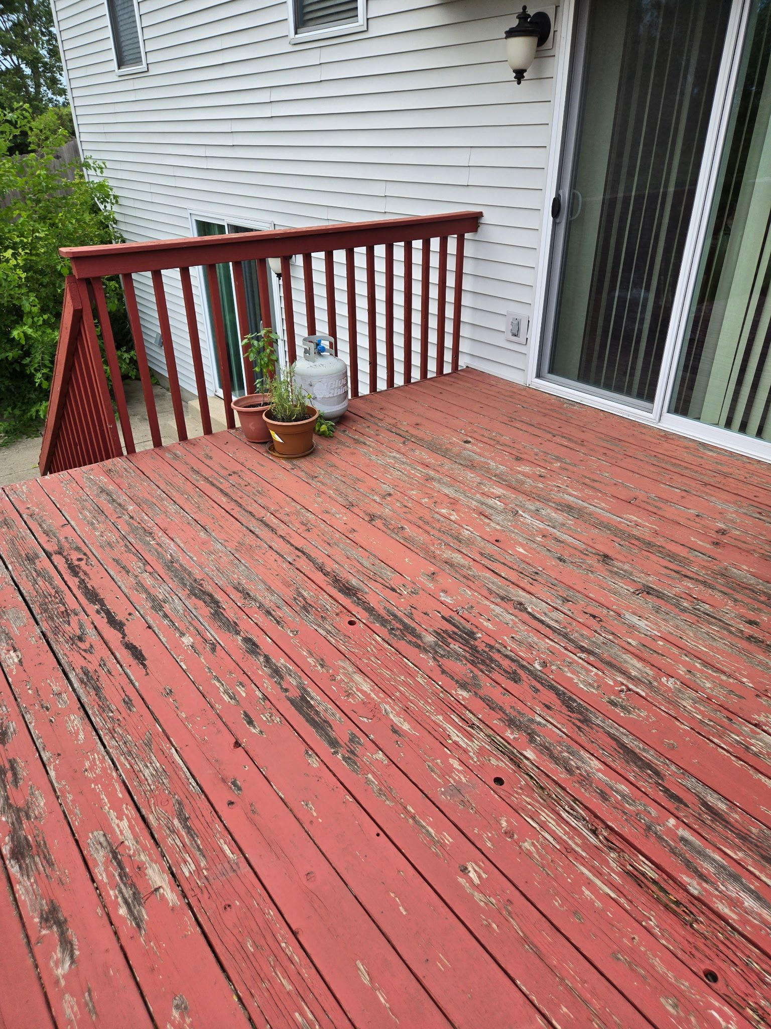 Red-painted wooden deck with peeling paint, railing, and sliding glass door to a white house.