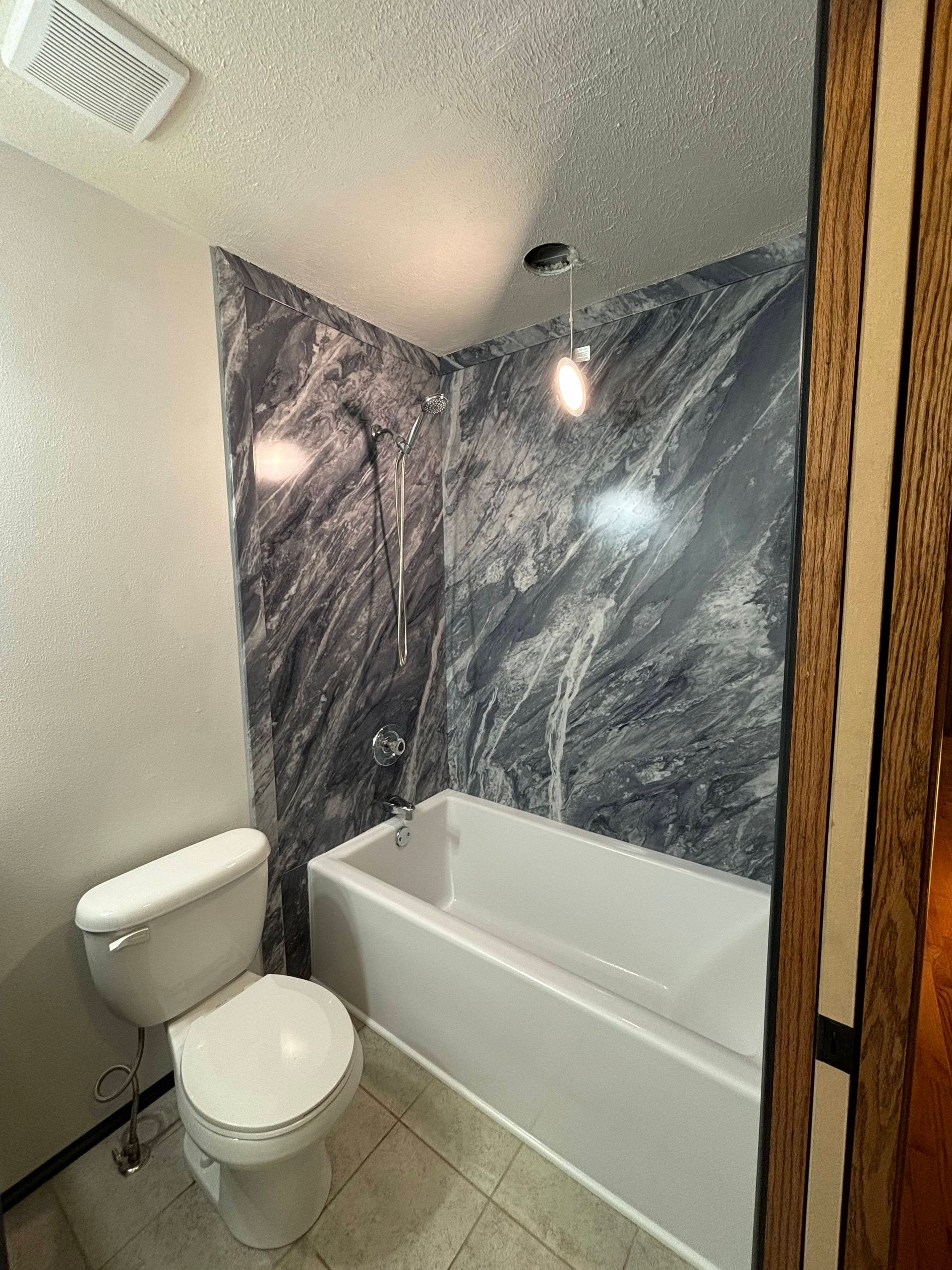 Bathroom with white toilet, bathtub, and gray marbled shower surround.