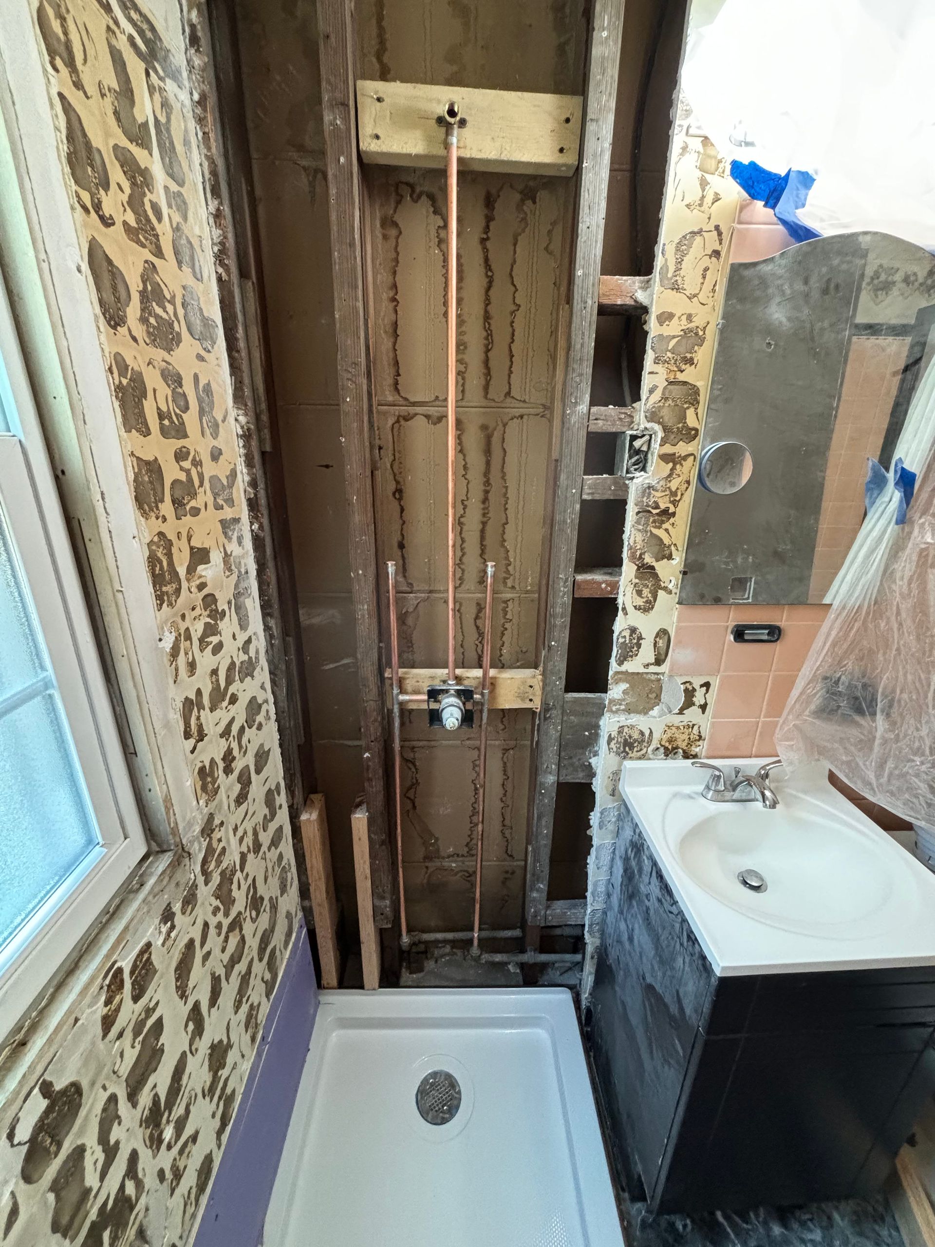 Bathroom renovation, copper plumbing installed in a wall cavity, shower base, sink, unfinished walls.