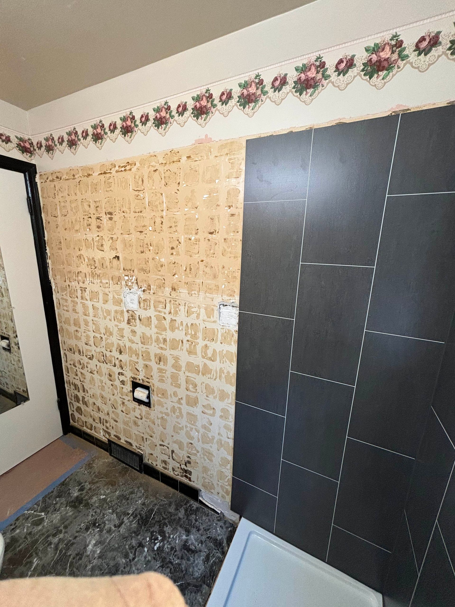 Wall with wallpaper partially removed, revealing textured surface; dark panel is installed.