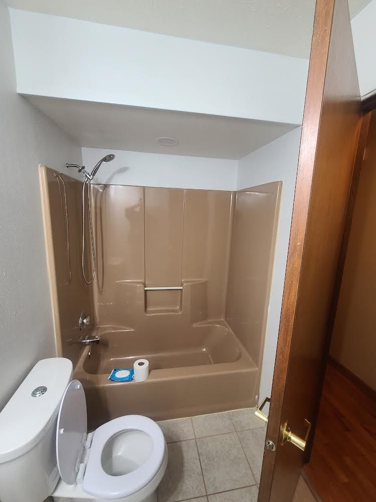 A small bathroom with a brown bathtub/shower, toilet, and partially visible door.