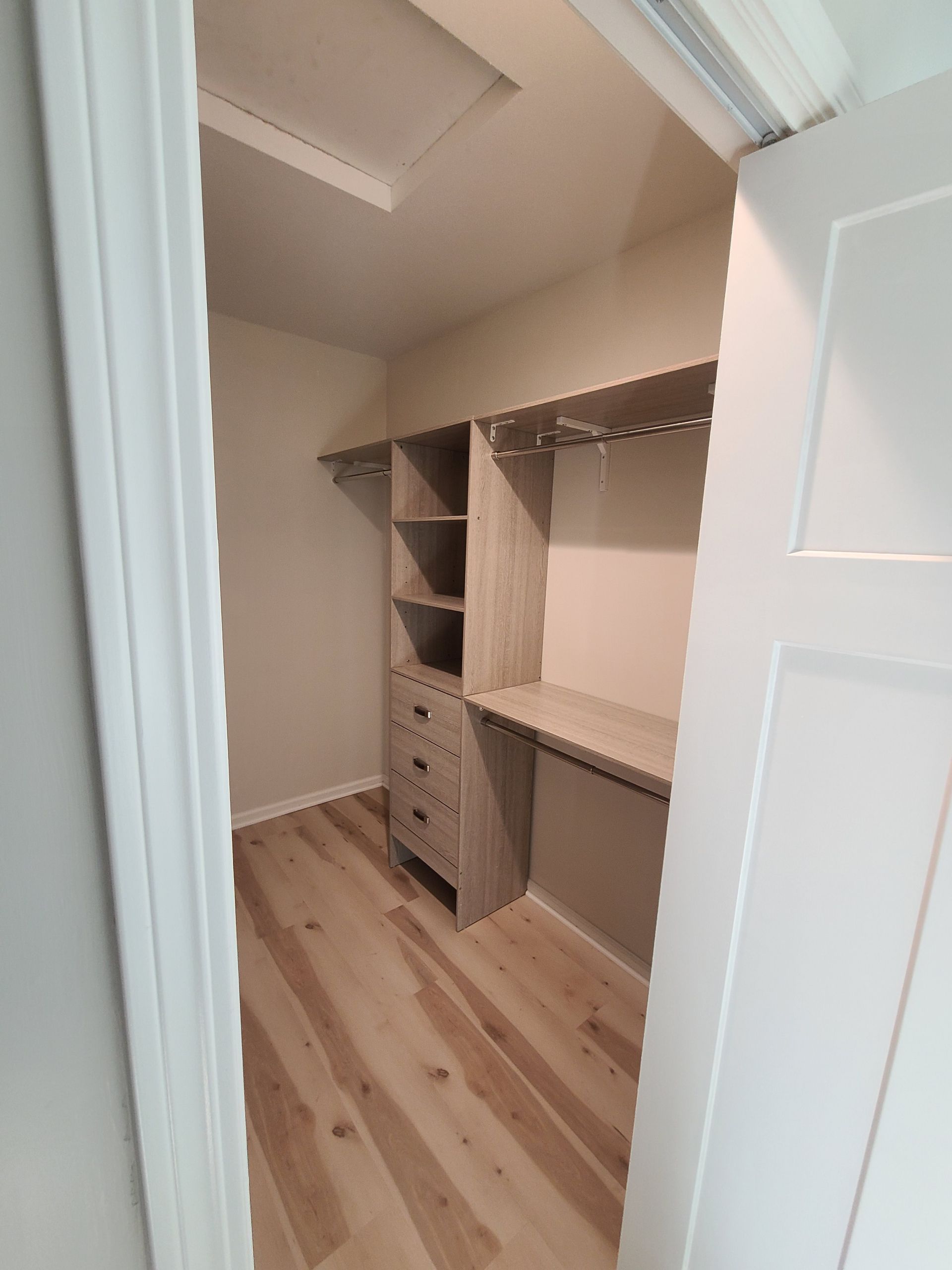 Walk-in closet with light wood flooring and built-in shelves, drawers, and hanging rods.