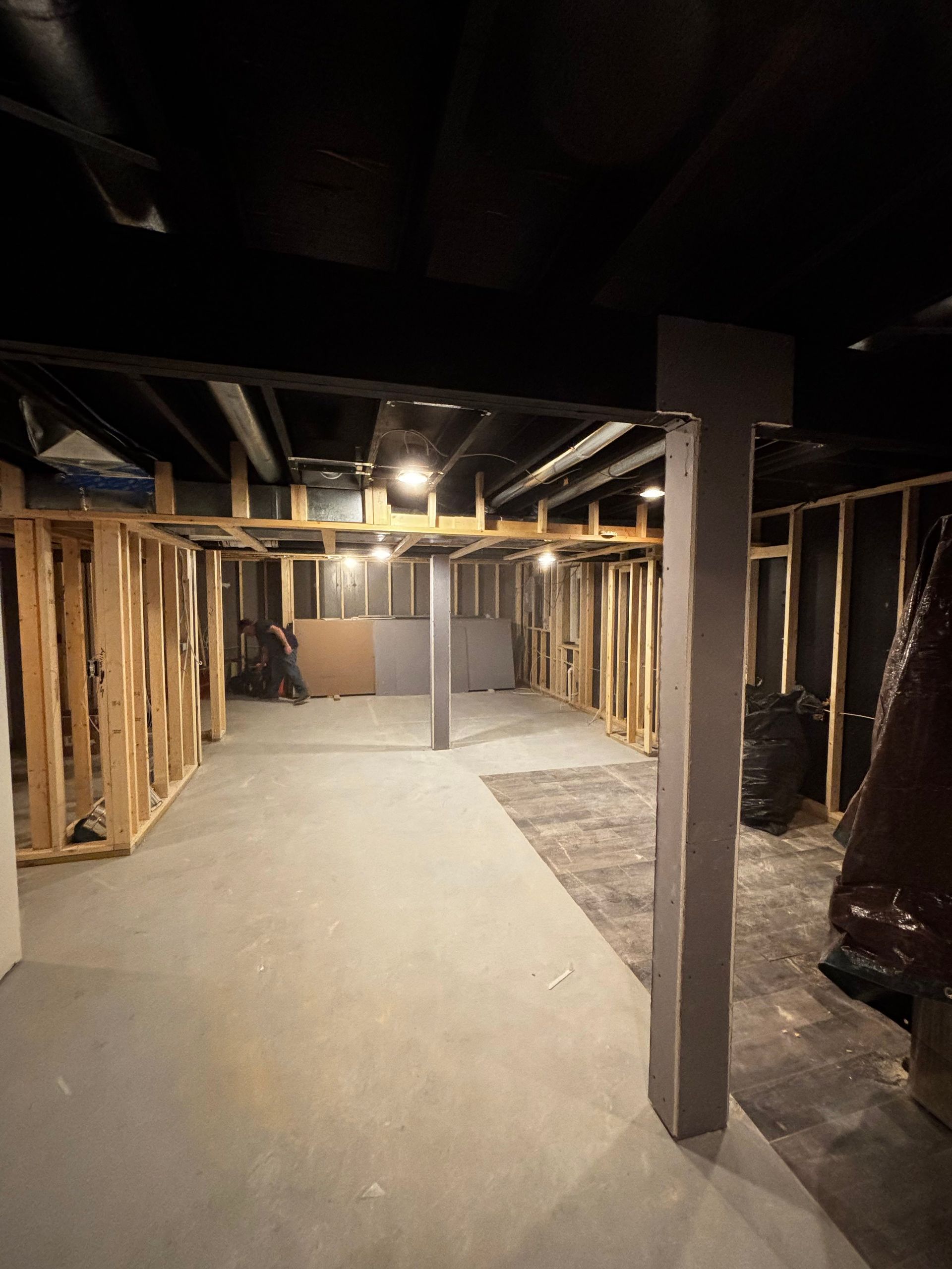 Unfinished basement with wooden studs, concrete floor, support pillars, and exposed ceiling beams.