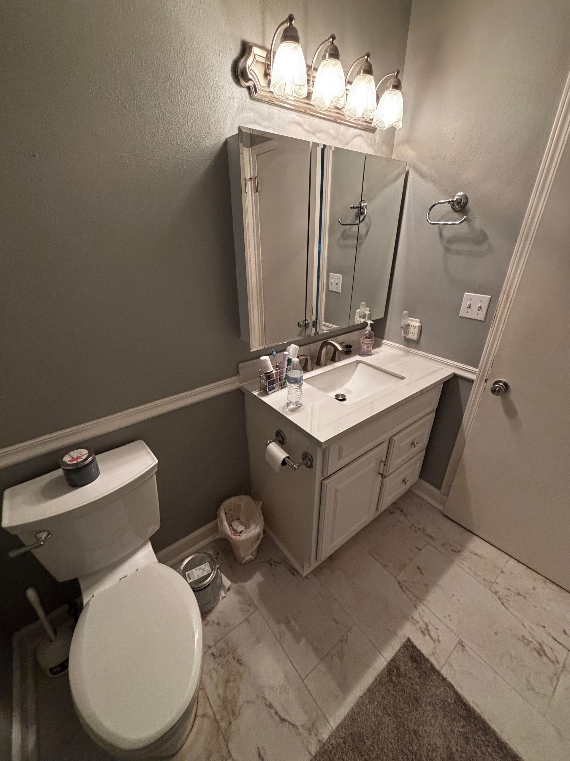 Bathroom with white sink, toilet, and vanity against gray walls, overhead light fixture, and marble-look flooring.