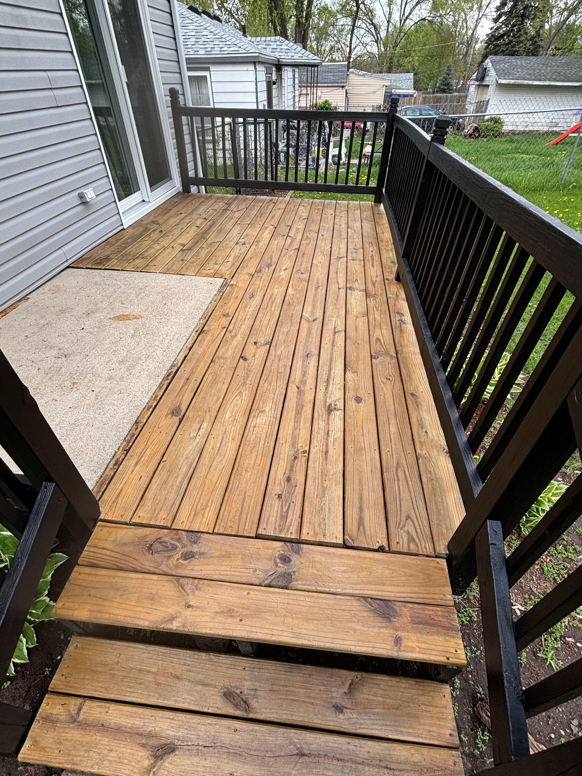 Wooden deck with dark railing and steps. Concrete area at the deck's edge.