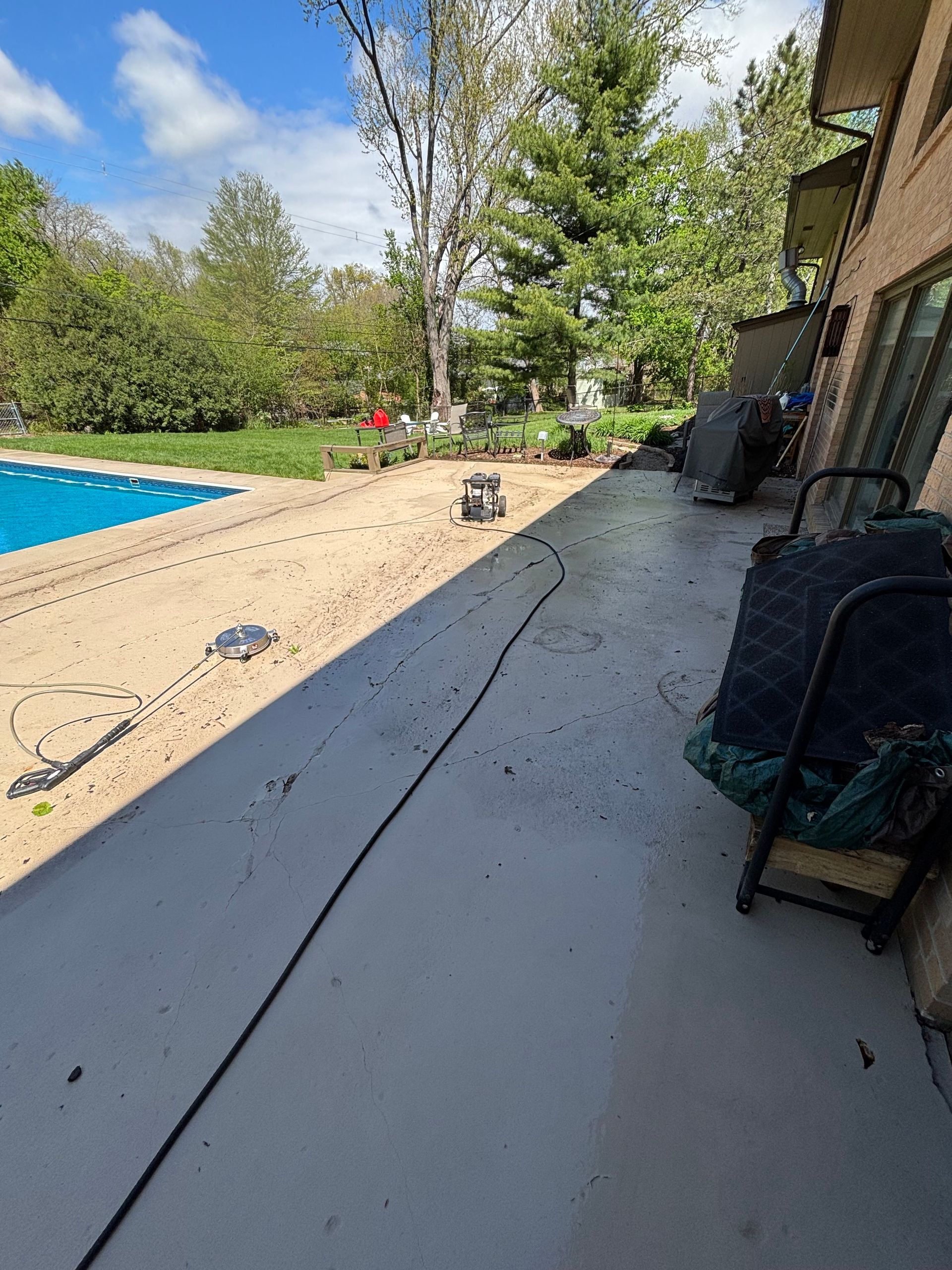 Concrete patio with a pool to the left. A power washer sits on the patio with a hose.