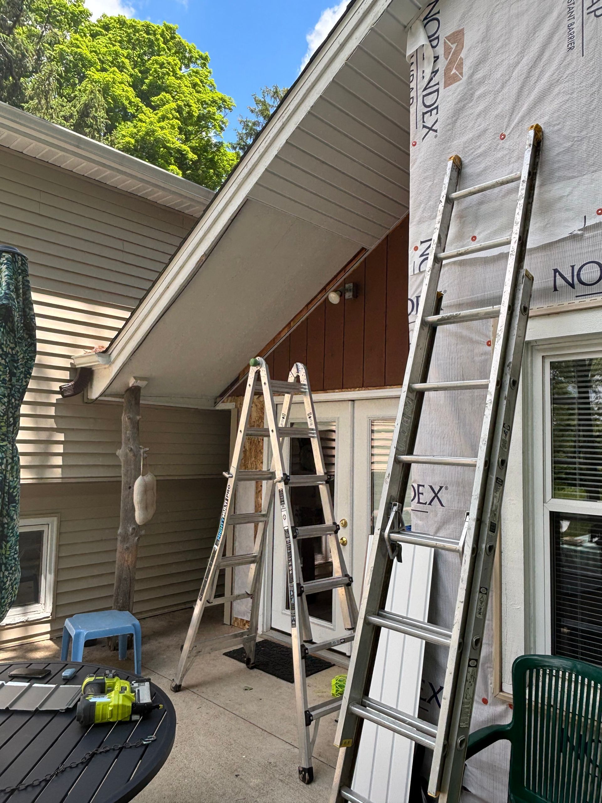 Three ladders leaning against a house during construction; brown siding and visible sheathing.