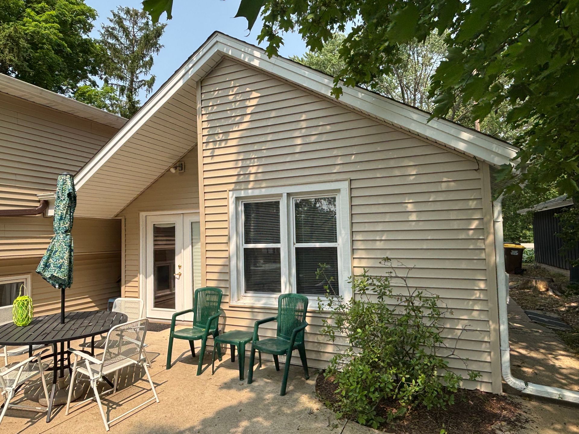 Beige house with a patio, green chairs, and round table.