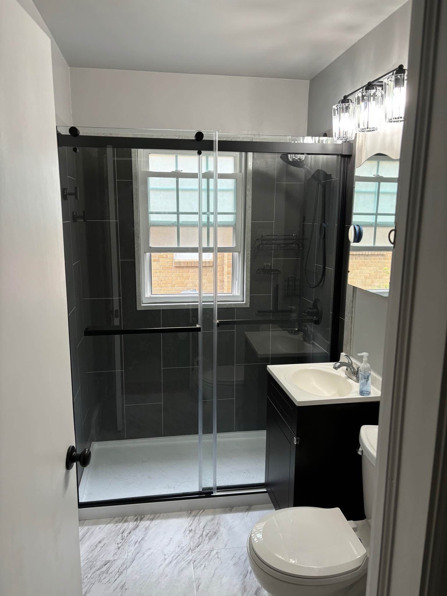 Bathroom with black shower enclosure, black vanity, white toilet, and window.