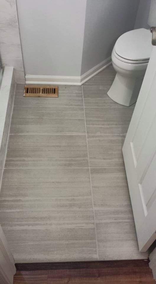 Bathroom floor with gray tiles, toilet, door, and vent. White trim, gray walls, and wood-like floor transition.