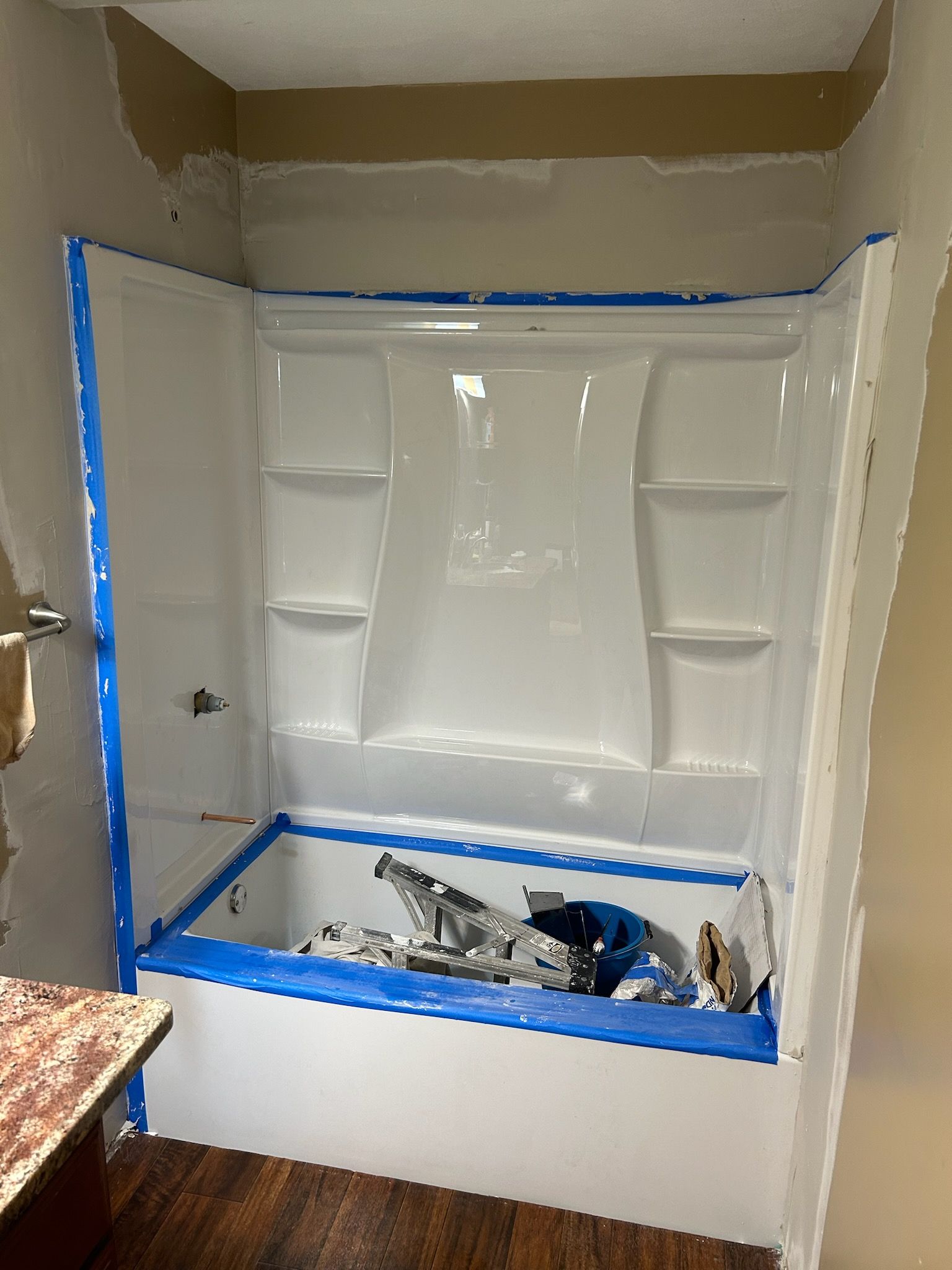 Bathroom remodel with new white tub/shower surround; blue tape, exposed wall, debris inside.