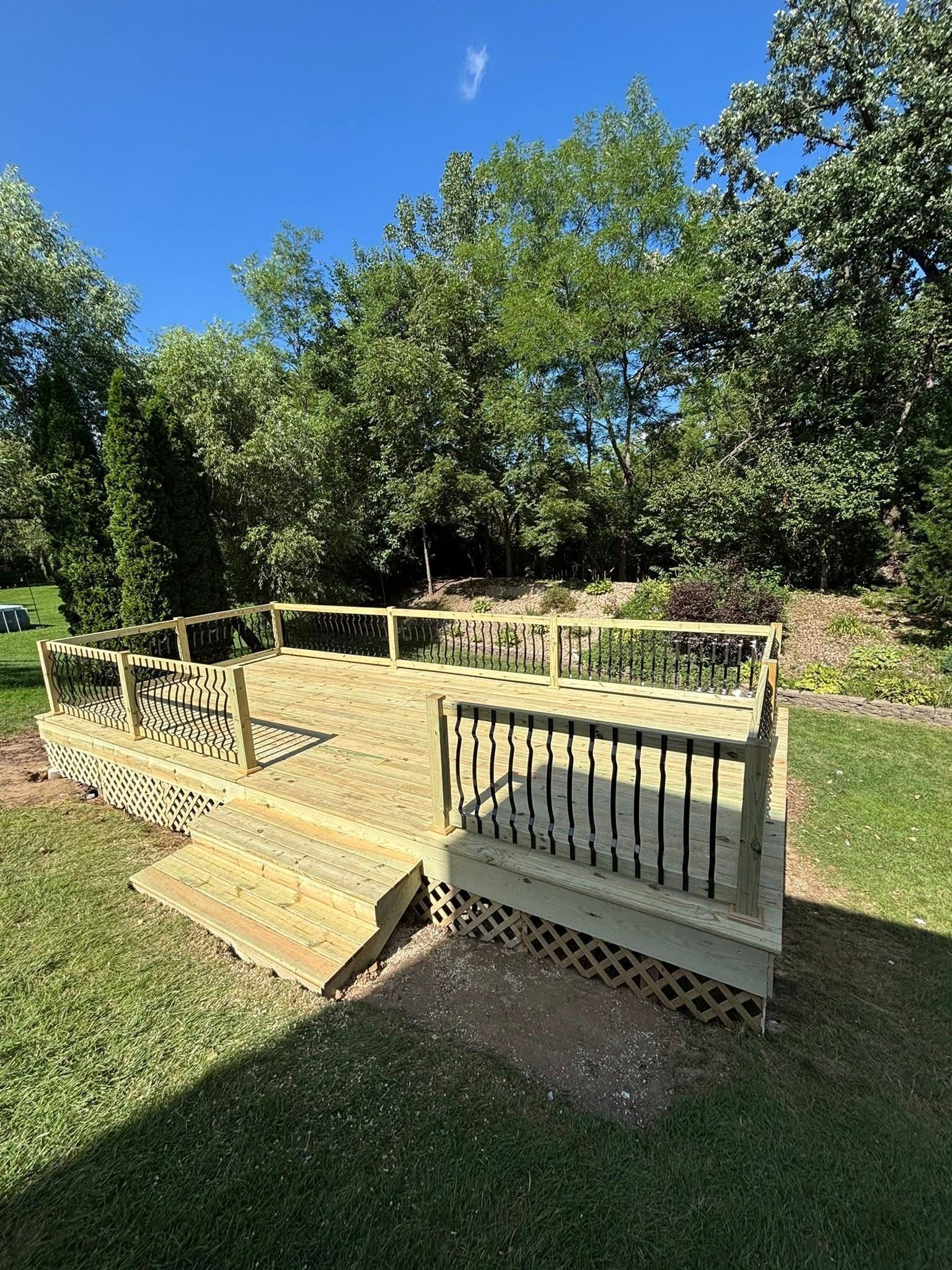 Wooden deck with steps and railing in a grassy backyard under a blue sky.