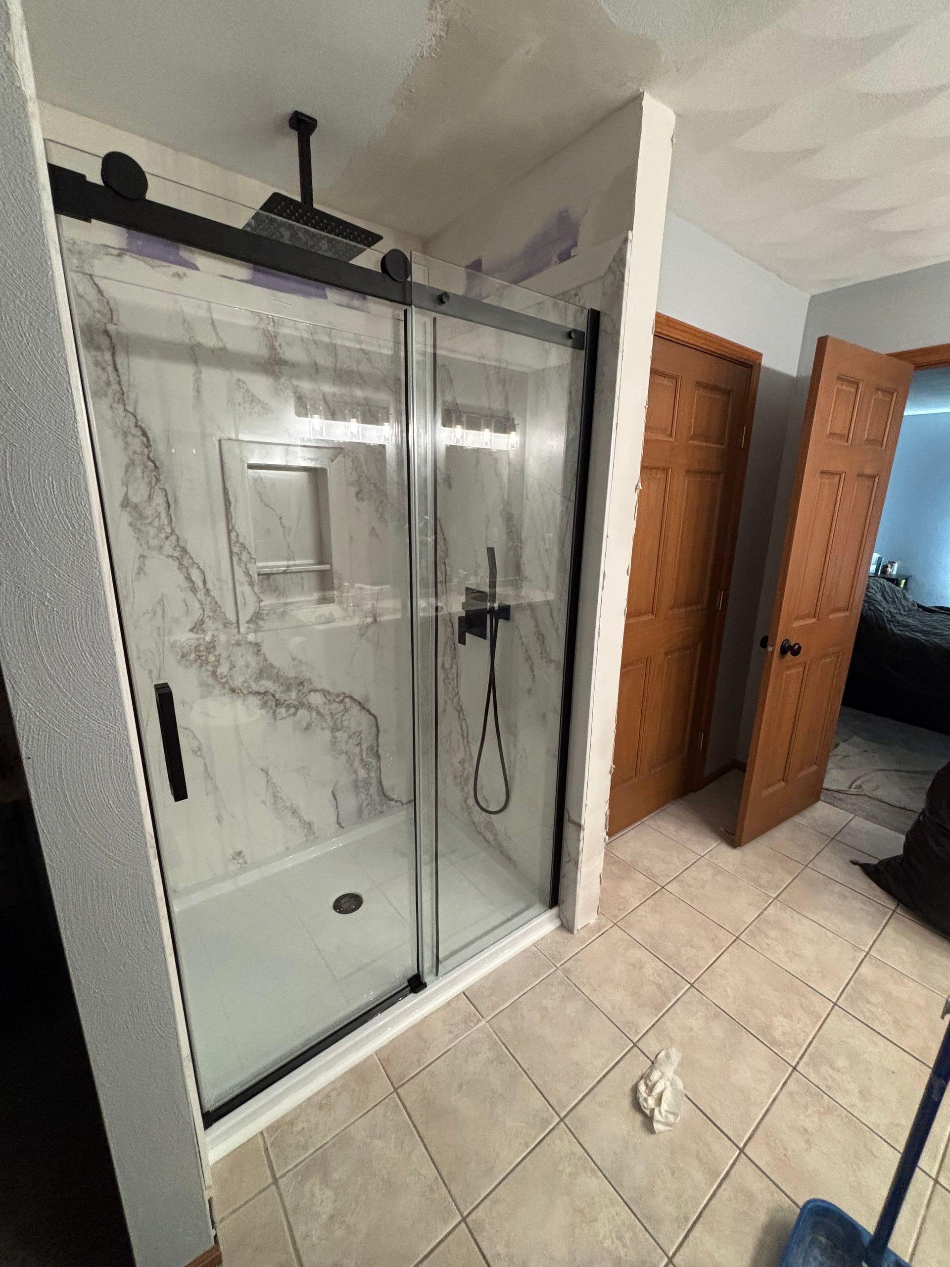 Modern shower enclosure with sliding glass doors, black hardware, marble-look wall panels, and a rain showerhead.