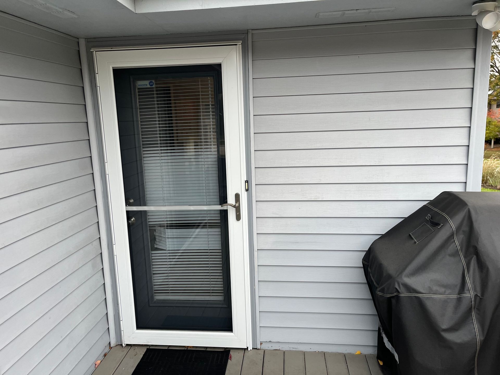Screen door on a gray-sided house exterior, next to a covered grill.