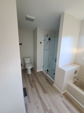 Bathroom interior: toilet, glass shower, light-colored wood floor, and neutral walls.