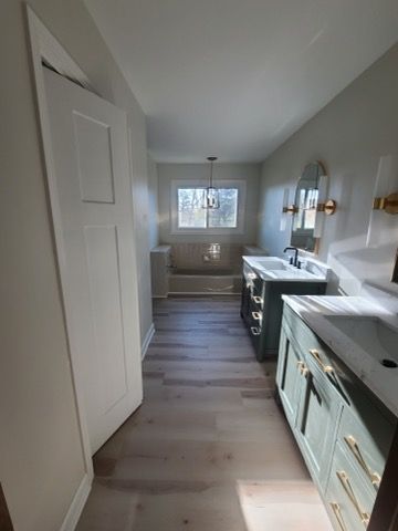 Bathroom with two teal vanities, white door, and a bathtub under a window.