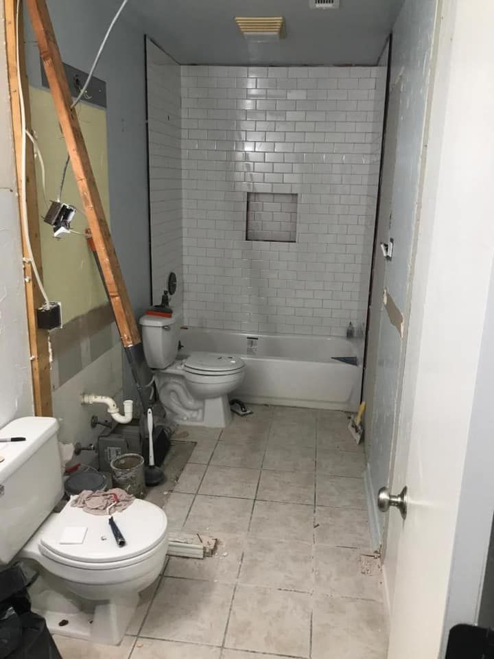 Bathroom undergoing renovation, with exposed walls, new tile, a toilet, and a bathtub.