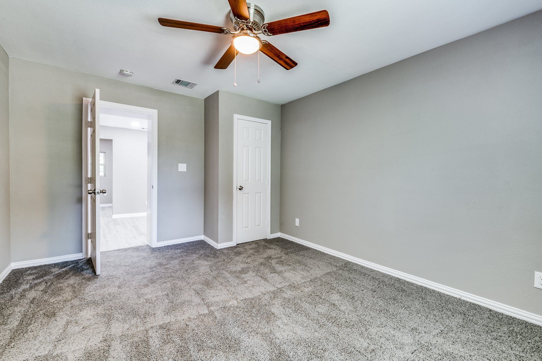 Empty bedroom with gray walls, carpet, ceiling fan, and open door to a bathroom.