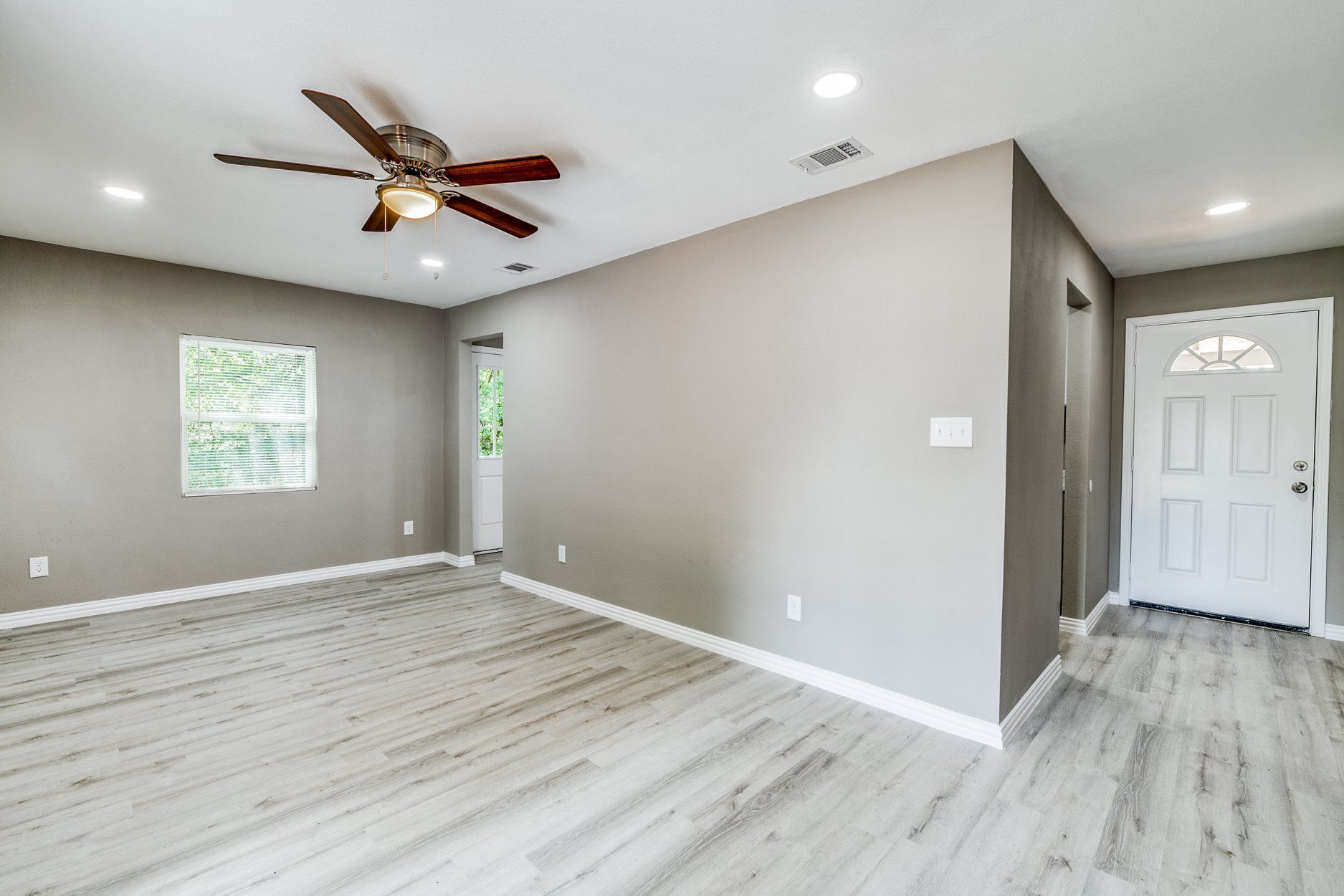 Living room with gray walls, light wood-look floors, white door, and a ceiling fan.