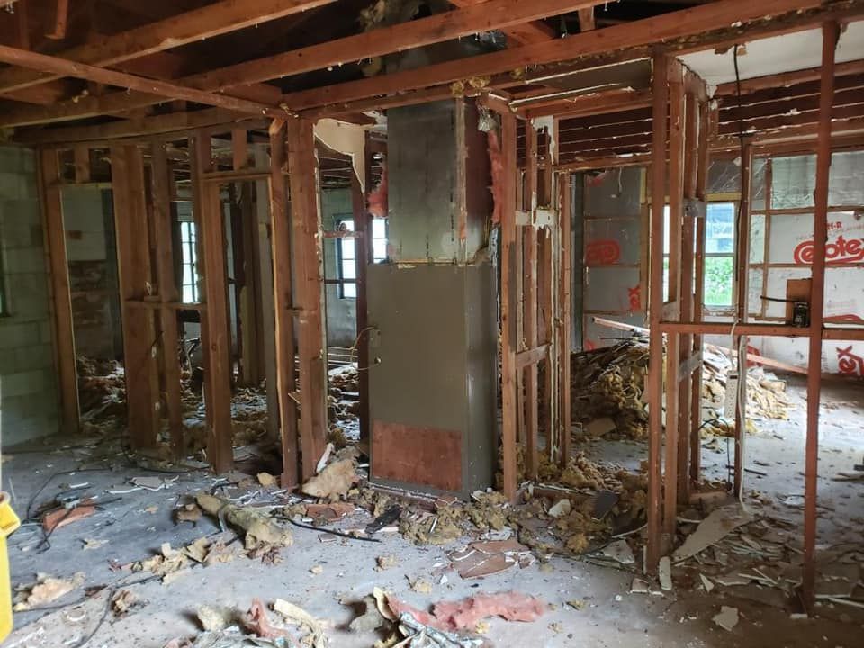 Interior view of a building under renovation, exposed wooden framing, insulation debris, concrete floor.