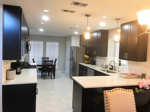 Modern kitchen with dark cabinets, white countertops, stainless steel appliances, and dining area.
