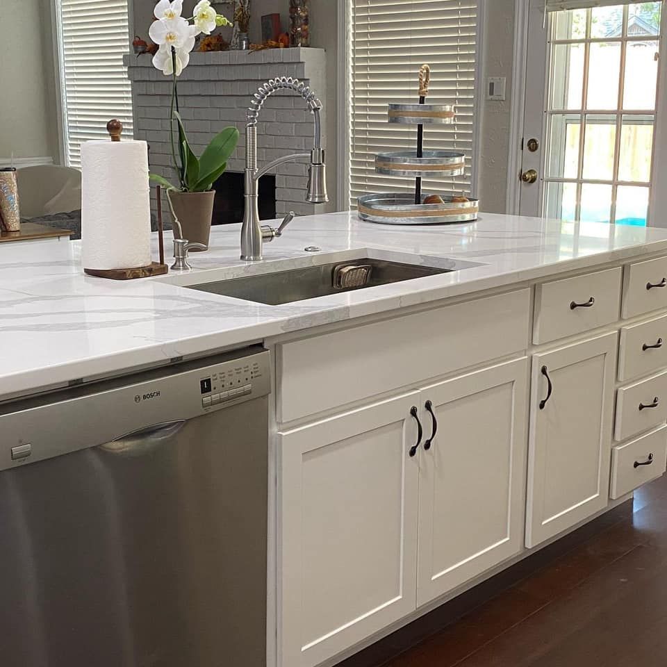 Kitchen island with white cabinets, stainless steel dishwasher, sink, and marble countertop.