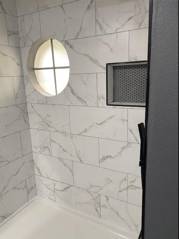 Tiled shower with marble-like pattern. An oval window and recessed shelf are set into the walls.