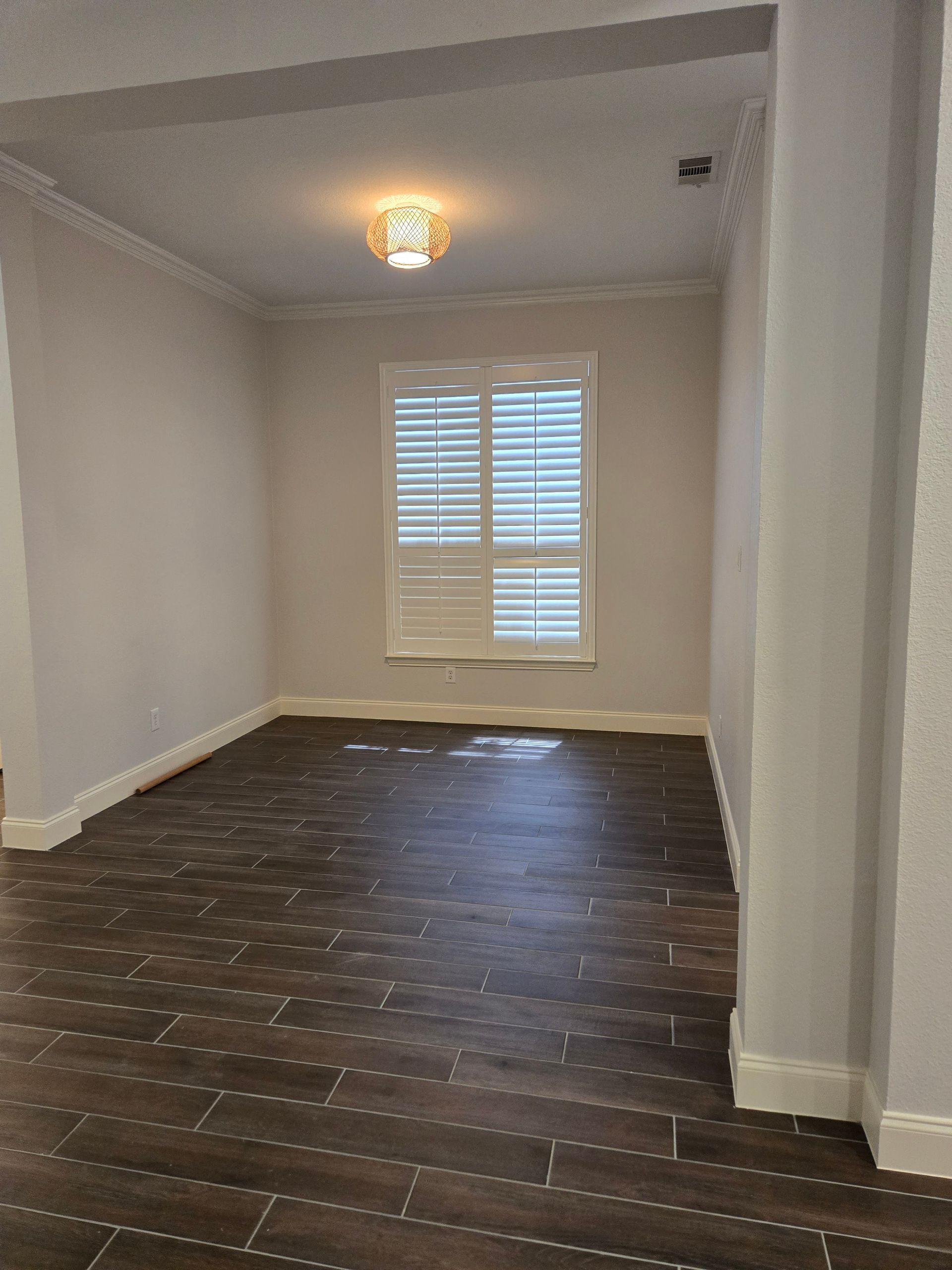 Empty room with wood-look tile flooring, white walls, window with shutters, and a decorative ceiling light.
