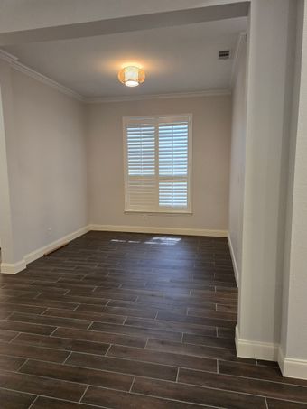 Empty room with wood-look tile flooring, white walls, window with shutters, and a decorative ceiling light.