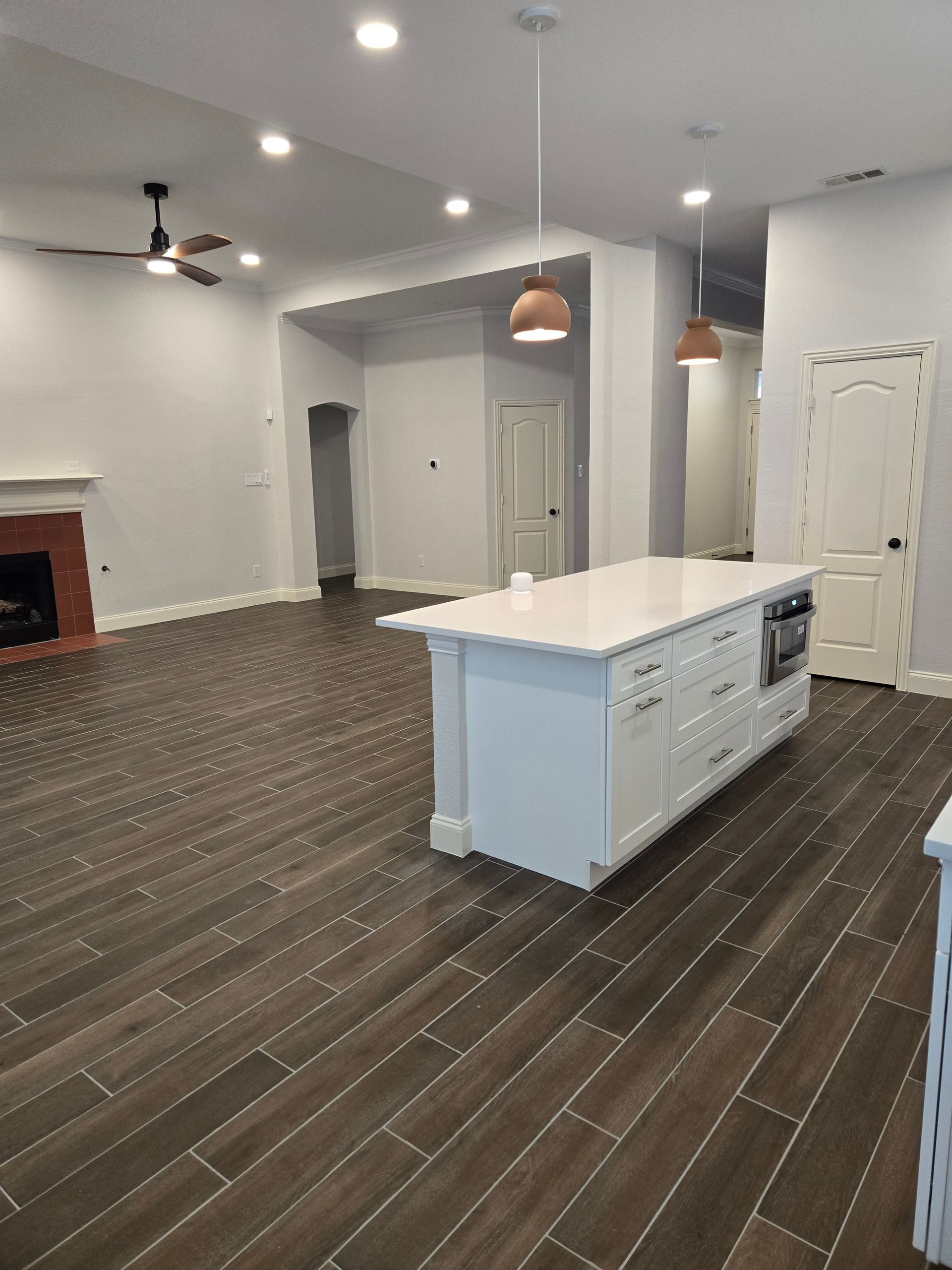 Open-concept living space with a white kitchen island, dark wood-look flooring, and a fireplace.