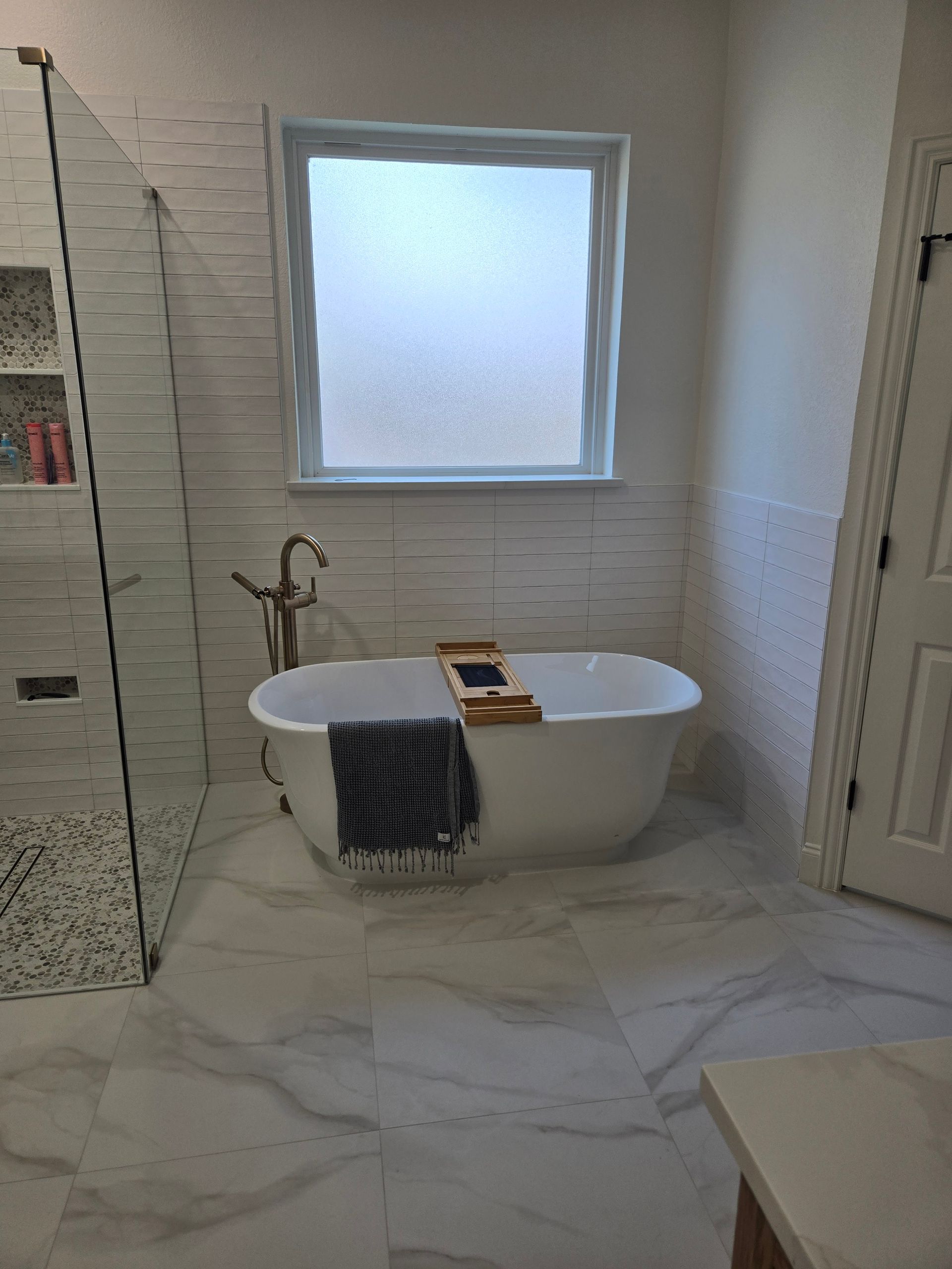 Elegant white bathroom with freestanding tub, window, and marble tile floor.
