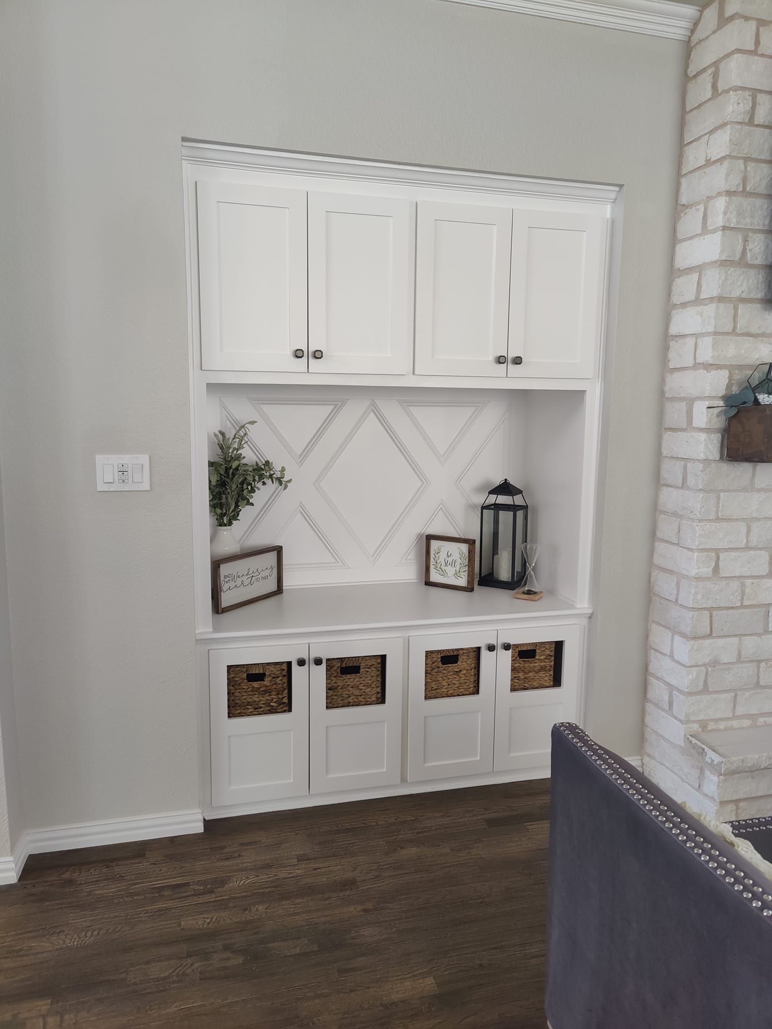 Built-in white cabinet unit with storage baskets, shelves, and upper cabinets, against a light gray wall.